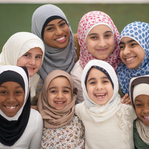 A very happy group of Muslim students posing with their teacher. They are all wearing a hijab or headscarf.